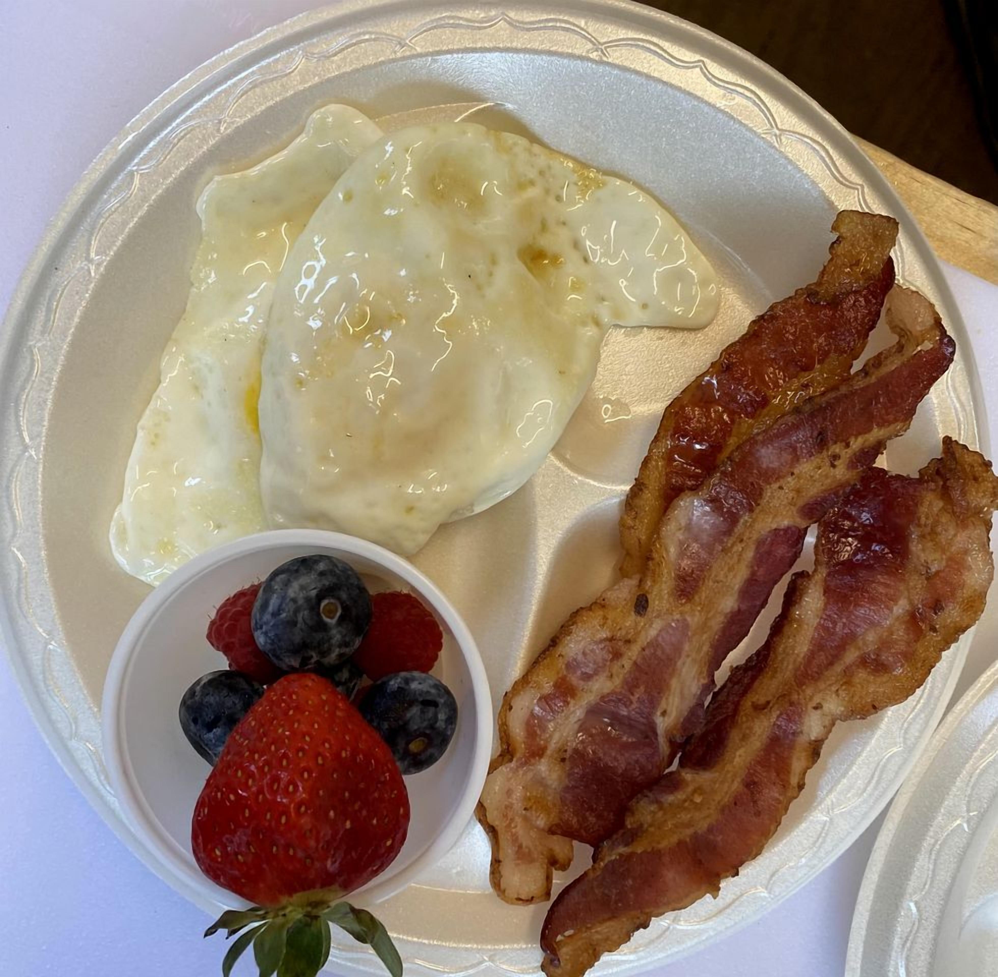 A plate with scrambled eggs, bacon, and a small bowl of berries.