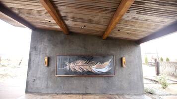 A concrete structure with a large abstract painting, wooden beams, and two wall-mounted light fixtures.