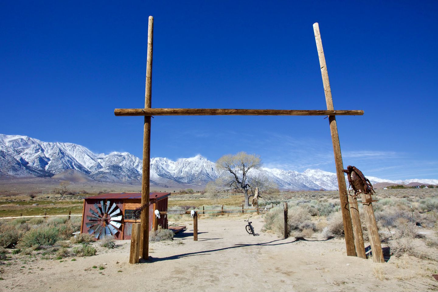 A rustic wooden structure with a windmill, a bicycle, and a bird perched on a post, set against a backdrop of snow-capped mountains.