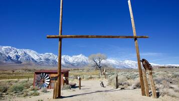 A rustic wooden structure with a windmill, a bicycle, and a bird perched on a post, set against a backdrop of snow-capped mountains.
