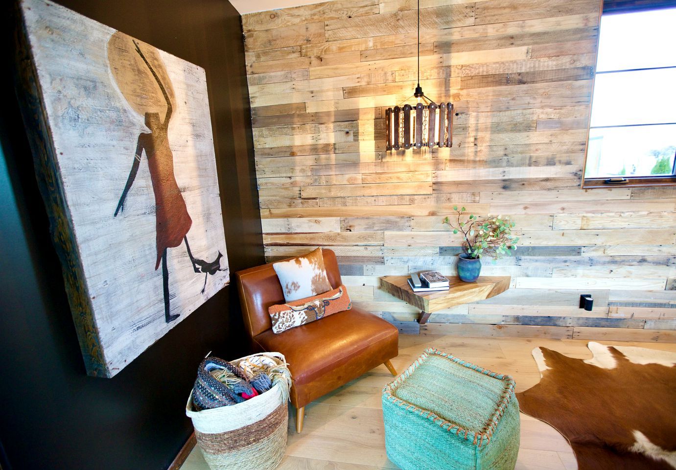 A modern living room with a wooden wall, a leather sofa, a hanging light fixture, and a cowhide rug.