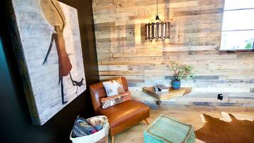 A modern living room with a wooden wall, a leather sofa, a hanging light fixture, and a cowhide rug.