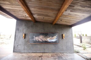 A concrete structure with a large abstract painting, wooden beams, and two wall-mounted light fixtures. - Luxury Design Rental with Breathtaking Mountain Views in Lone Pine, California (Lone Pine)