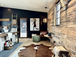 Un interior rústico con pared de madera, alfombra de cuero de vaca, un banco y un cuadro de una mujer.