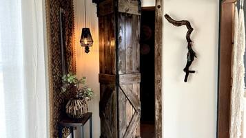 Un interior rústico con una puerta de madera, una lámpara colgante y una planta sobre una mesita.