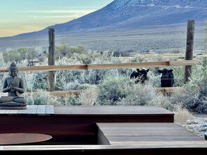 A wooden deck with a statue, a fence, and a mountainous landscape in the background. - Luxury Design Rental with Breathtaking Mountain Views in Lone Pine, California (Lone Pine)
