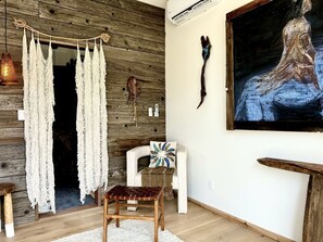 A room with a wooden wall, macrame curtains, a painting, a chair, and a small table. - Luxury Design Rental with Breathtaking Mountain Views in Lone Pine, California (Lone Pine)