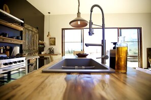 Una cocina con encimera de madera, un lavabo, una estufa y una lámpara colgante.