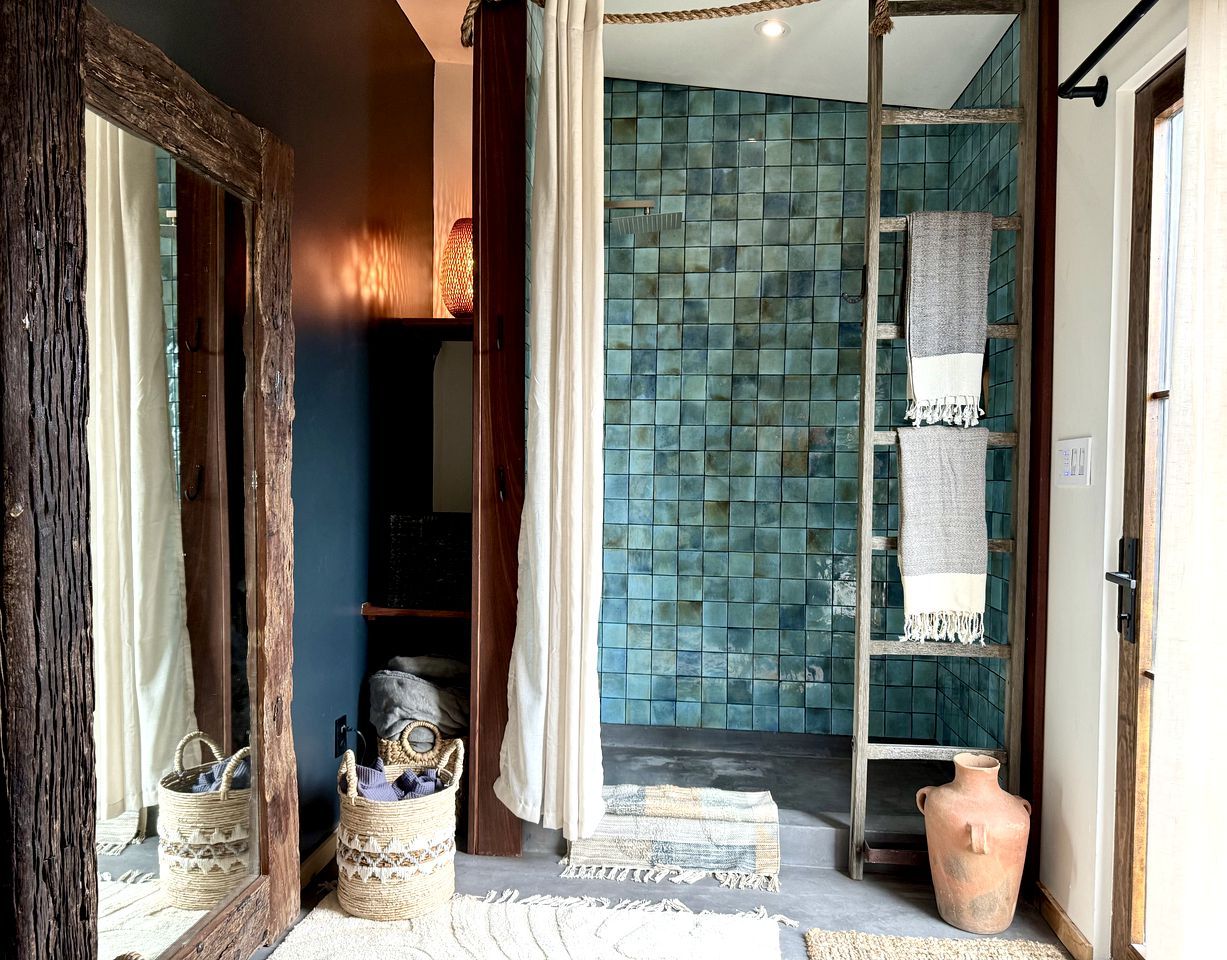 A room with a wooden door, a mirror, a woven basket, a tiled wall, and a small vase.