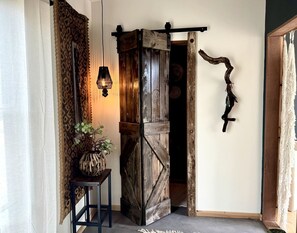 A rustic interior with a wooden door, a hanging light fixture, and a plant on a small table.