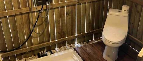 A wooden-fenced outdoor bathroom with a white toilet, a small sink, and a heater.