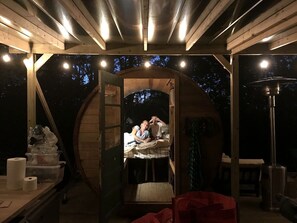 A rustic wooden structure with a loft bed, a small table with items, and a large barrel.