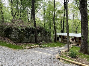 Un chalet rustique avec une allée en gravier, entouré d’une forêt dense.