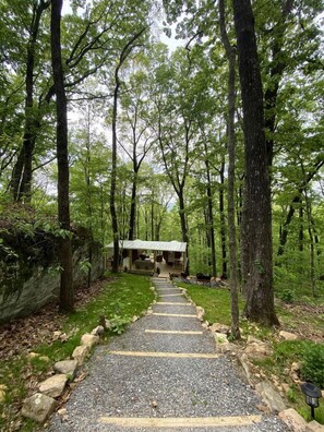 A forested area with a gravel pathway leading to a cabin-like structure.