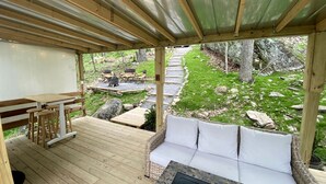 Una terraza al aire libre con una mesa y sillas de madera, un banco acolchado y un hogar de piedra.