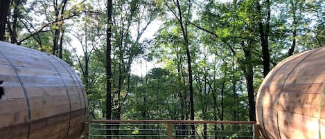 A wooden barrel-shaped room with a metal railing and a view of a forest.