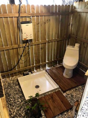 A wooden-fenced outdoor bathroom with a white toilet, a small sink, and a heater.