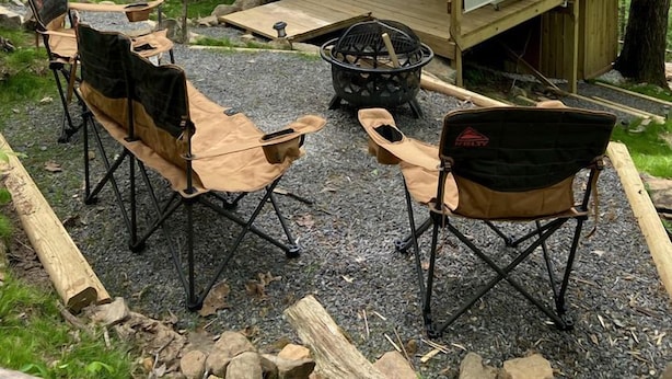 Een rustieke hut met een terras, zitplaatsen buiten en een vuurkuil.