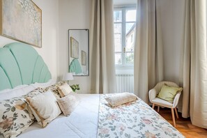 Ein Schlafzimmer mit Bett, Stuhl, Fenster und Bildern an den Wänden.