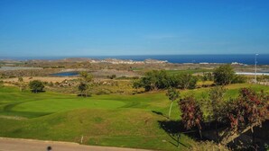 A golf course with a view of the ocean and distant buildings.