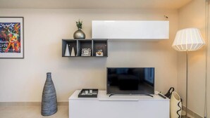 A modern living room with a flat-screen TV, a white entertainment unit, a floor lamp, and a decorative vase.