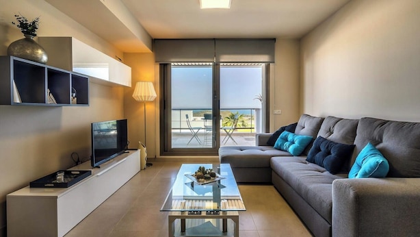 A modern living room with a sofa, TV, and a glass coffee table.