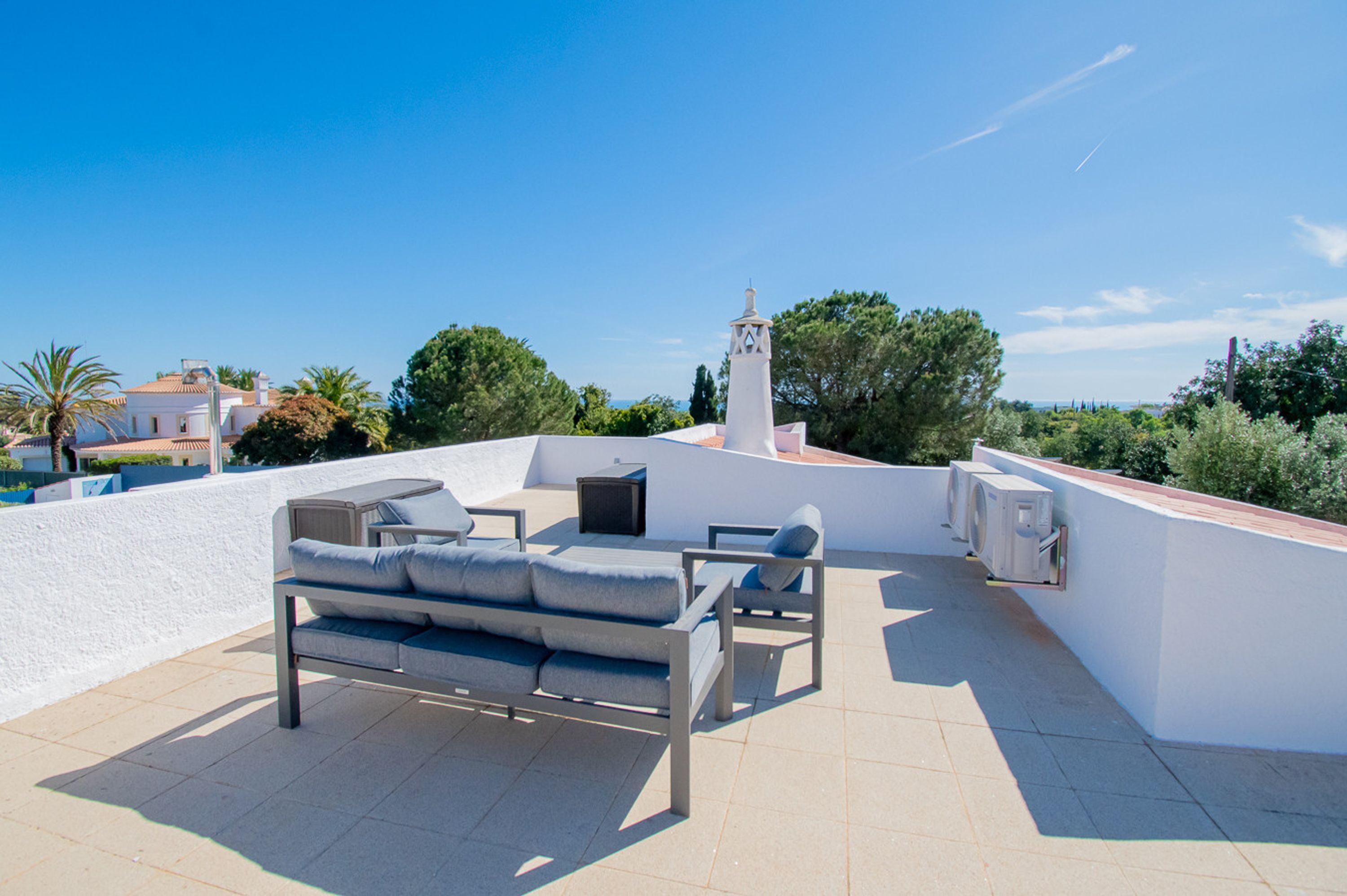 A rooftop terrace with a sofa, chairs, and a small table.
