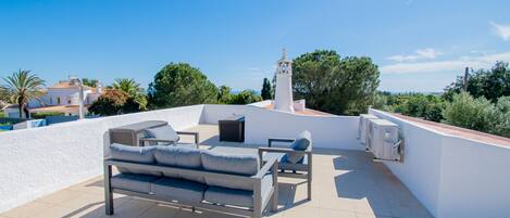 A rooftop terrace with a sofa, chairs, and a small table.
