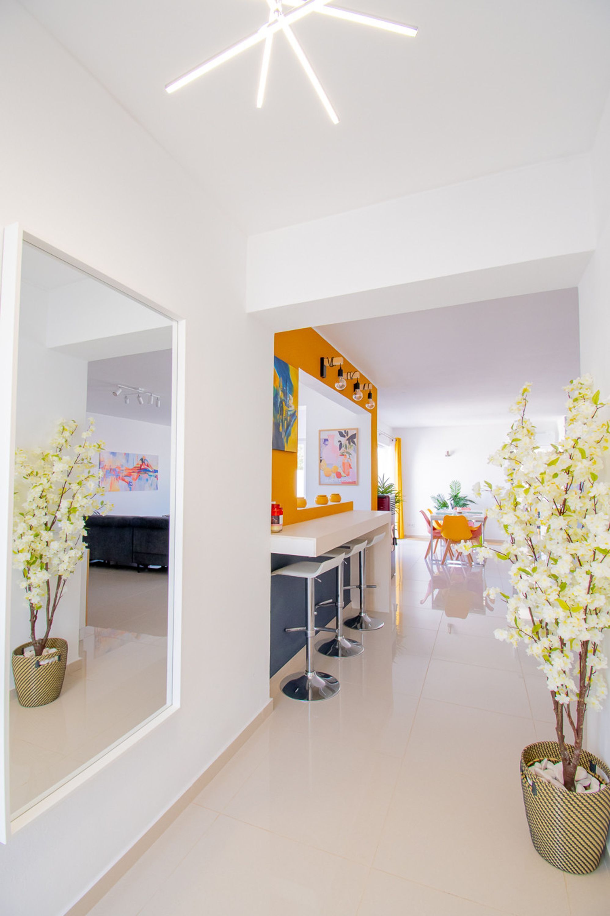 A modern interior with a kitchen area, a dining space, and a hallway with potted plants.