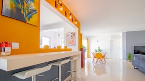 Una cocina moderna con barra, zona de comedor con mesa y sillas, y sala de estar con sofá.
