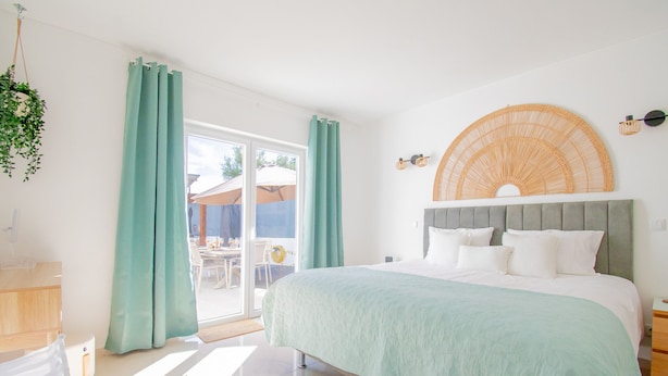 Un dormitorio con cama, cortinas, una planta colgante y vistas al exterior.