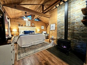 Une pièce confortable avec un lit, une petite table, une lampe, une cheminée et un ventilateur de plafond.
