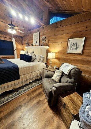 Una habitación acogedora con cama, una silla, una mesita de noche y techo de madera.