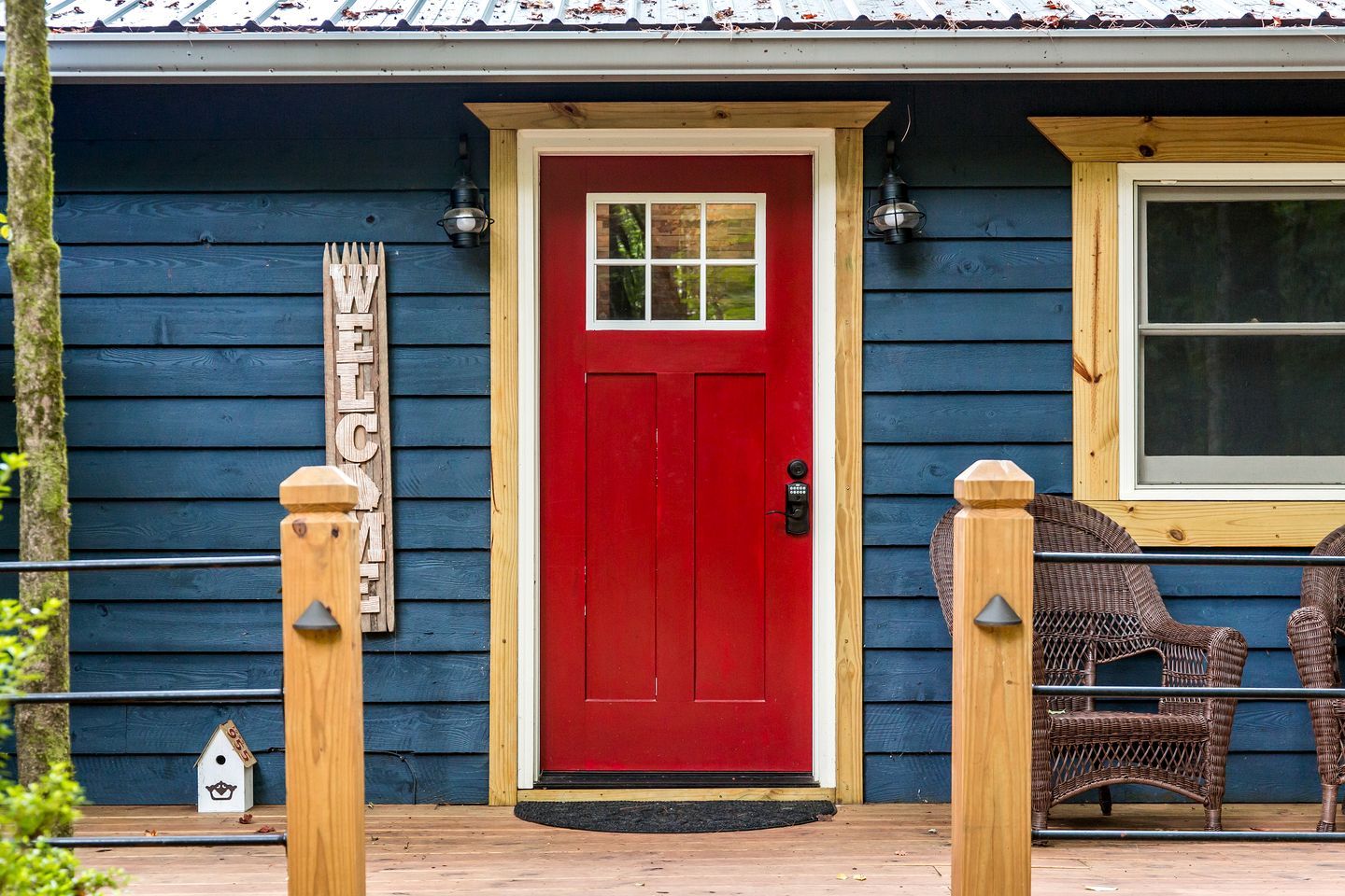 A red door with a window, a 'WELCOME' sign, and wicker furniture outside.