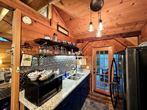 A kitchen with a microwave, sink, and refrigerator, wooden ceiling, and a window with a view. - Romantic Creekside Cabin Retreat with Hot Tub, Fire Pit and Peaceful Forest Views in Sautee Nacoochee, Georgia (Sautee Nacoochee)