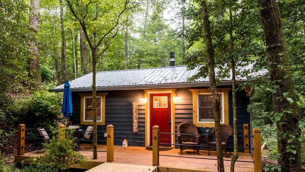 A cabin with a wooden deck, a red door, and wicker chairs outside. - Romantic Creekside Cabin Retreat with Hot Tub, Fire Pit and Peaceful Forest Views in Sautee Nacoochee, Georgia (Sautee Nacoochee)