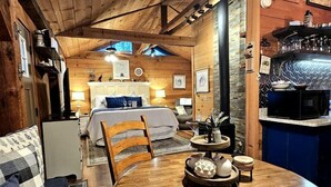 Accogliente interno di una baita con tavolo da pranzo in legno, divano, letto e angolo cottura.