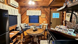 Un interno accogliente di una baita, con un tavolo da pranzo in legno, sedie, un frigorifero e un angolo caffè.