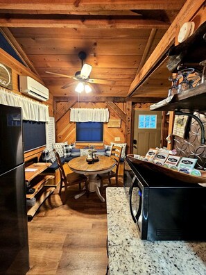 A cozy cabin interior with a wooden dining table, chairs, a refrigerator, and a coffee station. - Romantic Creekside Cabin Retreat with Hot Tub, Fire Pit and Peaceful Forest Views in Sautee Nacoochee, Georgia (Sautee Nacoochee)