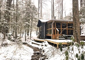 A cabin with a wooden deck, a small porch, and a window overlooking a forested area. - Romantic Creekside Cabin Retreat with Hot Tub, Fire Pit and Peaceful Forest Views in Sautee Nacoochee, Georgia (Sautee Nacoochee)
