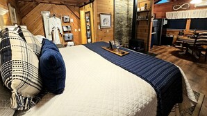 A cozy room with a bed, a wooden ceiling, a stone wall, and a dining area. - Romantic Creekside Cabin Retreat with Hot Tub, Fire Pit and Peaceful Forest Views in Sautee Nacoochee, Georgia (Sautee Nacoochee)