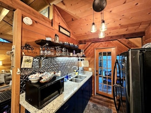 A kitchen with a microwave, sink, and refrigerator, wooden ceiling, and a window with a view. - Romantic Creekside Cabin Retreat with Hot Tub, Fire Pit and Peaceful Forest Views in Sautee Nacoochee, Georgia (Sautee Nacoochee)