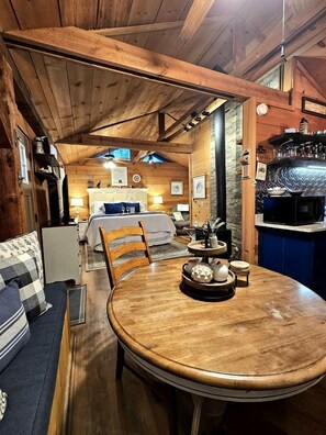 Een gezellig interieur van een blokhut met een houten eettafel, een bank, een bed en een keukenhoek.