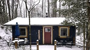 A cabin with a red door, a small porch, and a snow-covered deck. - Romantic Creekside Cabin Retreat with Hot Tub, Fire Pit and Peaceful Forest Views in Sautee Nacoochee, Georgia (Sautee Nacoochee)