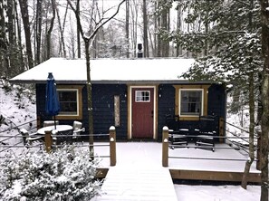 Una cabaña con puerta roja, un porche pequeño y una terraza cubierta de nieve.