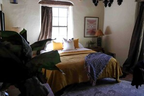 A bedroom with a bed, a window, a lamp, and a painting on the wall. - Casita Mistica a Southwest Adobe Cottage, Nogal, NM (Nogal)