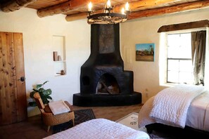 A rustic room with a stone fireplace, two beds, a wicker chair, and a window with curtains.