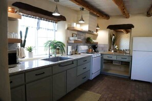 A kitchen with a sink, stove, and refrigerator, wooden beams on the ceiling, and a window with plants. - Casita Mistica a Southwest Adobe Cottage, Nogal, NM (Nogal)