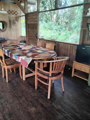A wooden dining area with a round table, chairs, and a large window overlooking greenery.