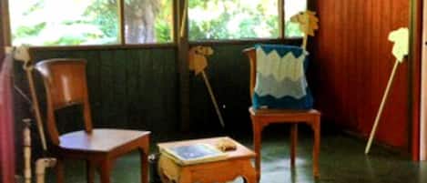 Une pièce avec une grande fenêtre, une chaise en bois, une petite table et un tapis à motifs.